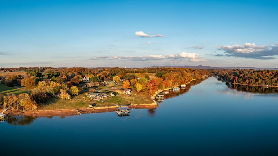 A calm lake with autumn foliage, a dock, and houses along the shore.