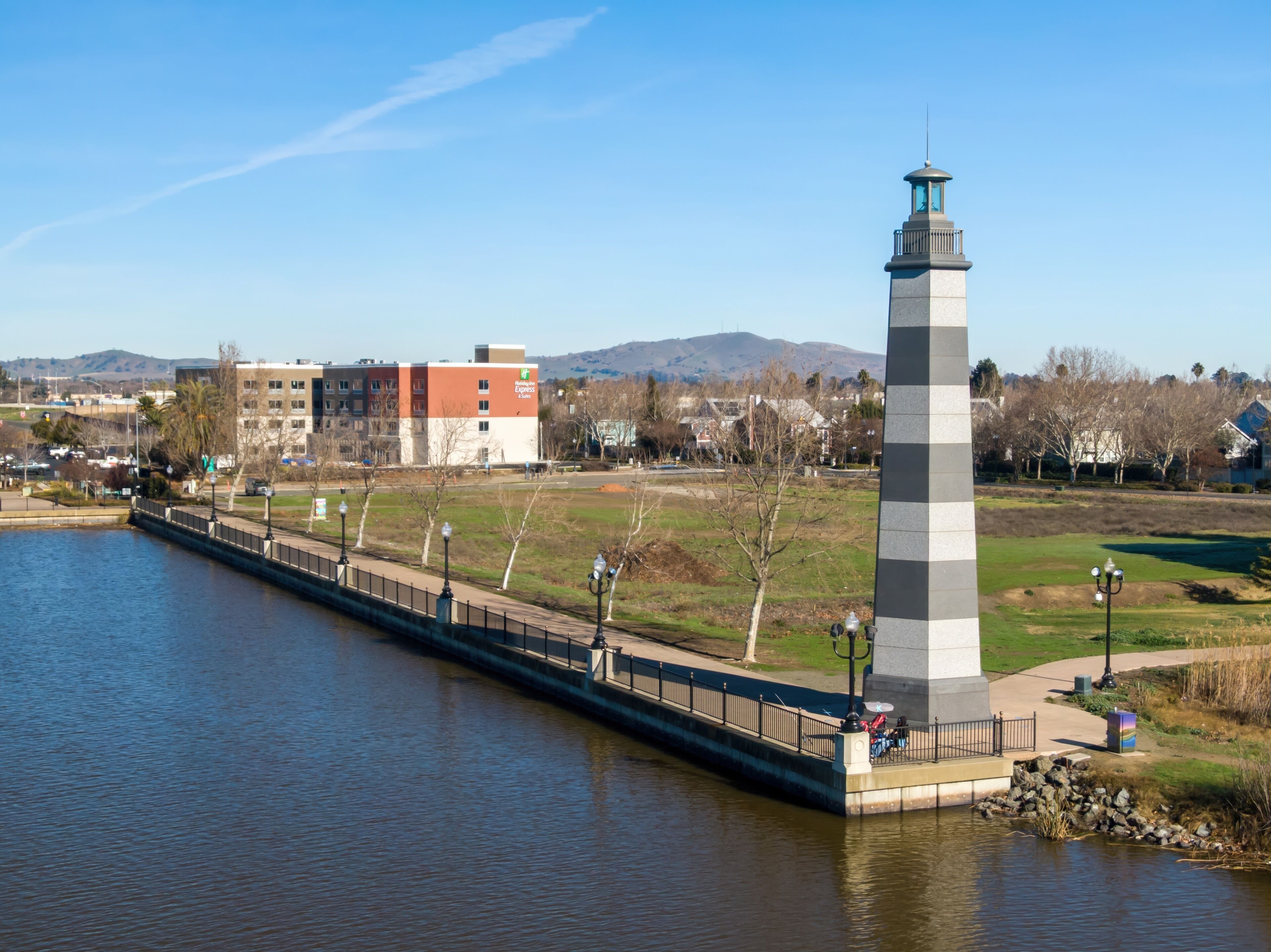 The Suisun City lighthouse in California, USA, stands tall on a pier along the waterfront. People relax nearby, enjoying the view of the water and the surrounding landscape.