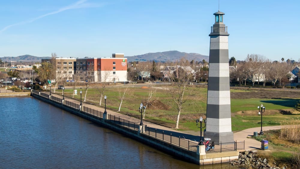 A lighthouse by a river, a bridge, and a park with trees.