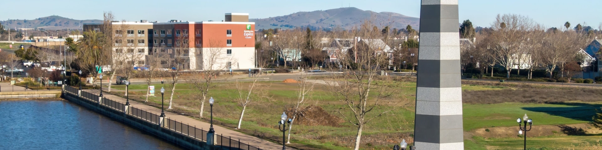 Un faro junto a un río, un puente y un parque con árboles.