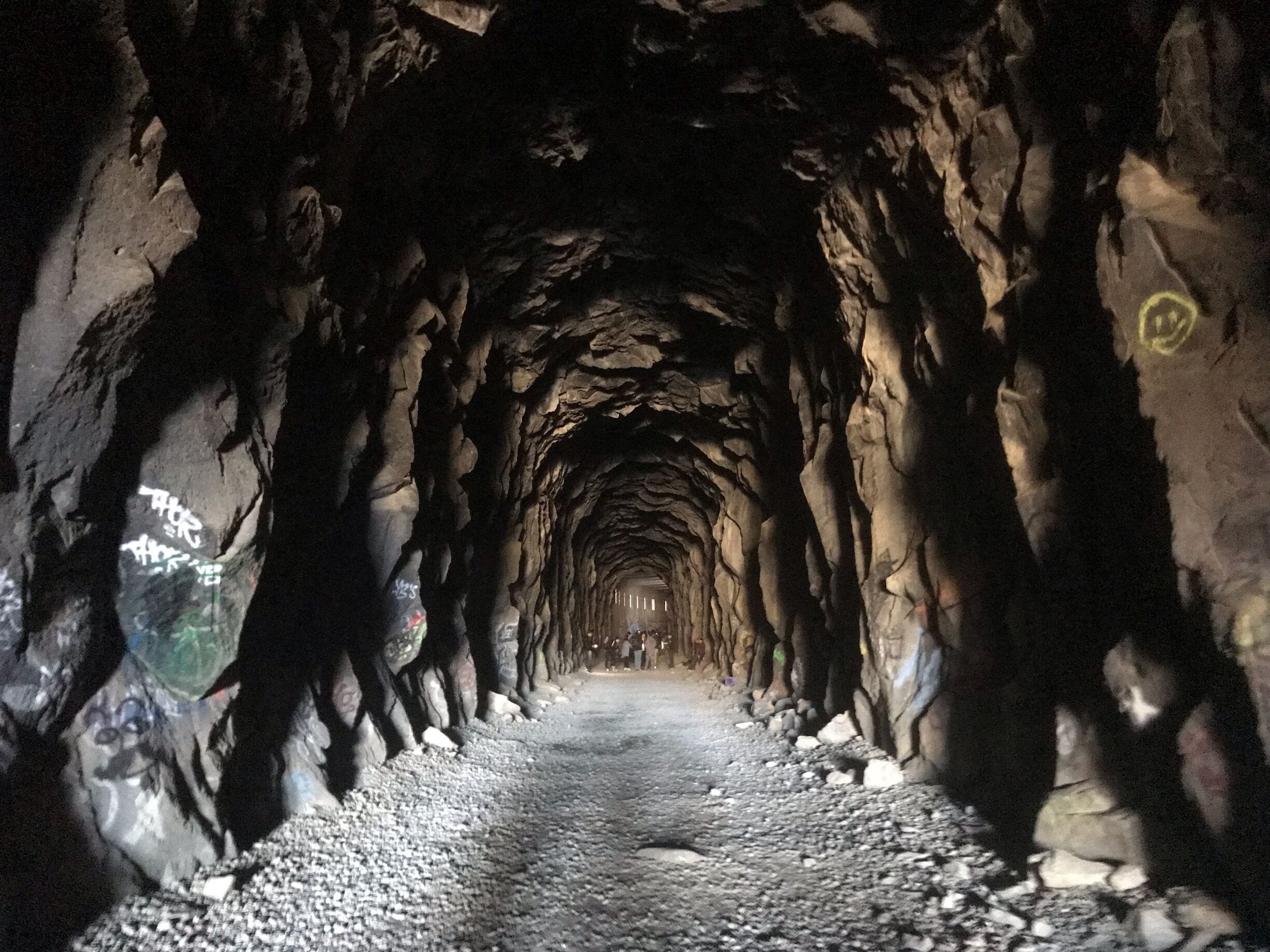 Un túnel con paredes rugosas e irregulares, con grafitis.