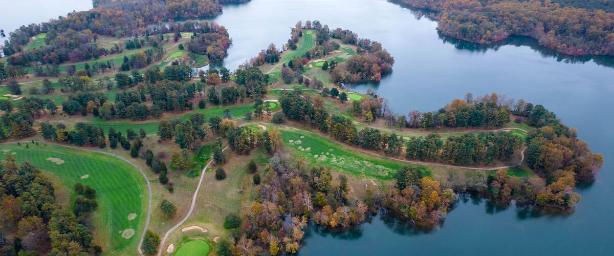 An aerial view of a golf course surrounded by a lake and forested areas.