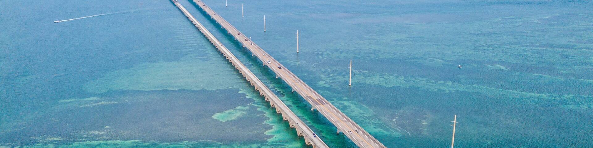 An aerial view of a long bridge over a turquoise sea with clear waters and a distant island.