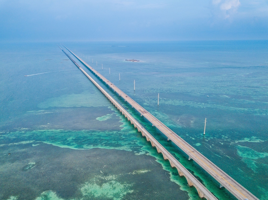 Vista aérea de uma longa ponte sobre um mar azul-turquesa, águas cristalinas e uma ilha distante.