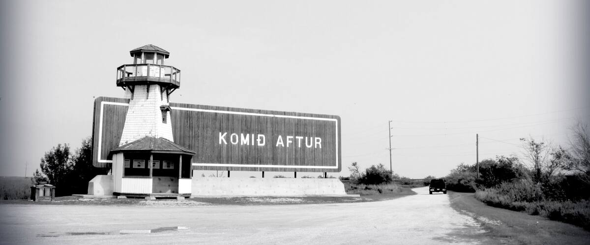 A lighthouse and a building with the text "KOMID AFTUR" on its facade.