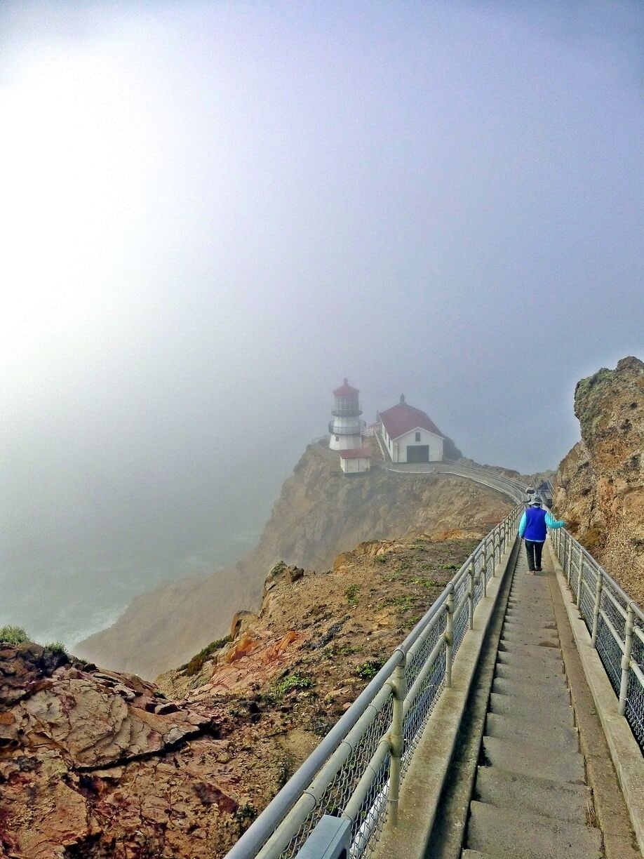 A person walking on a stone staircase leading to a lighthouse on a cliff.