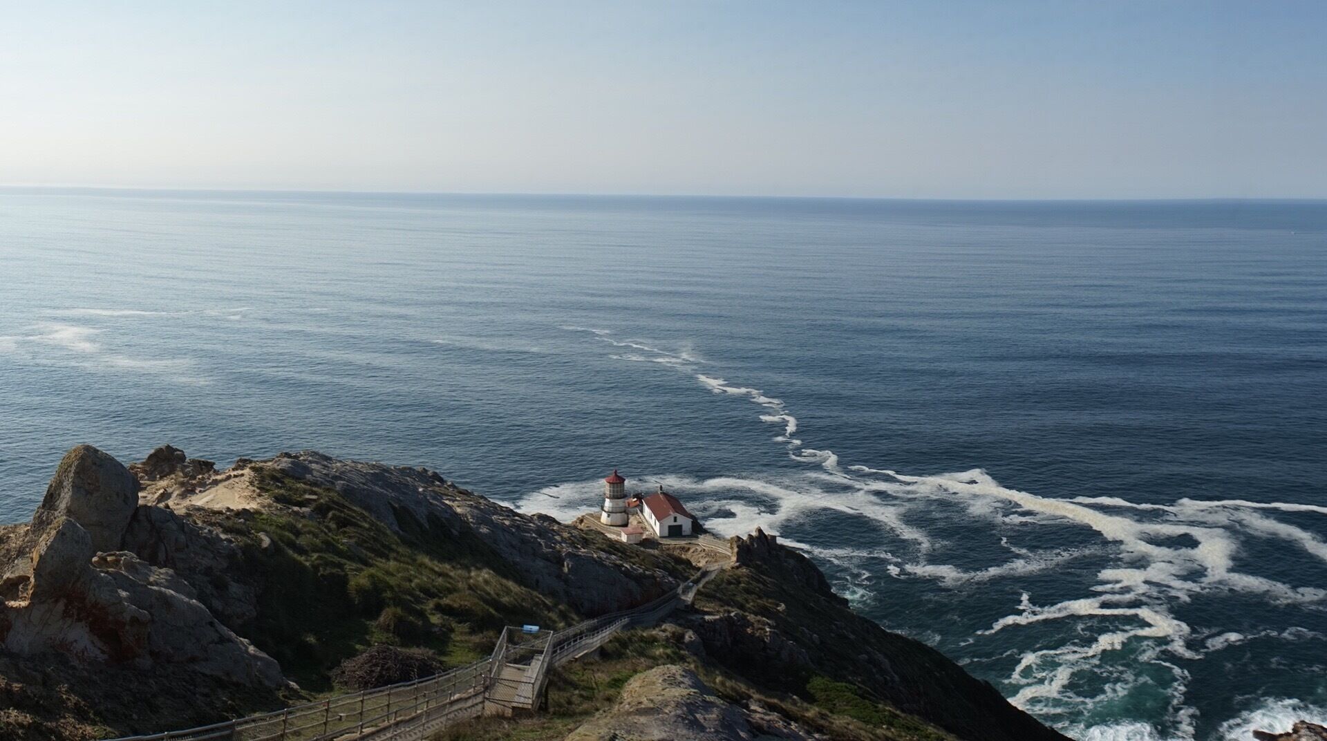 A coastal landscape with a lighthouse, rocky cliffs, and a sea view.