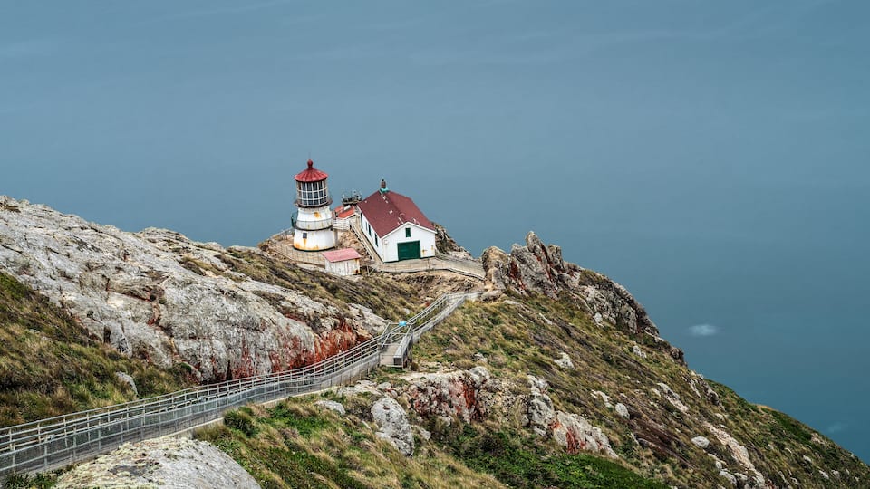 A lighthouse and a small building on a rocky cliff overlooking the sea.