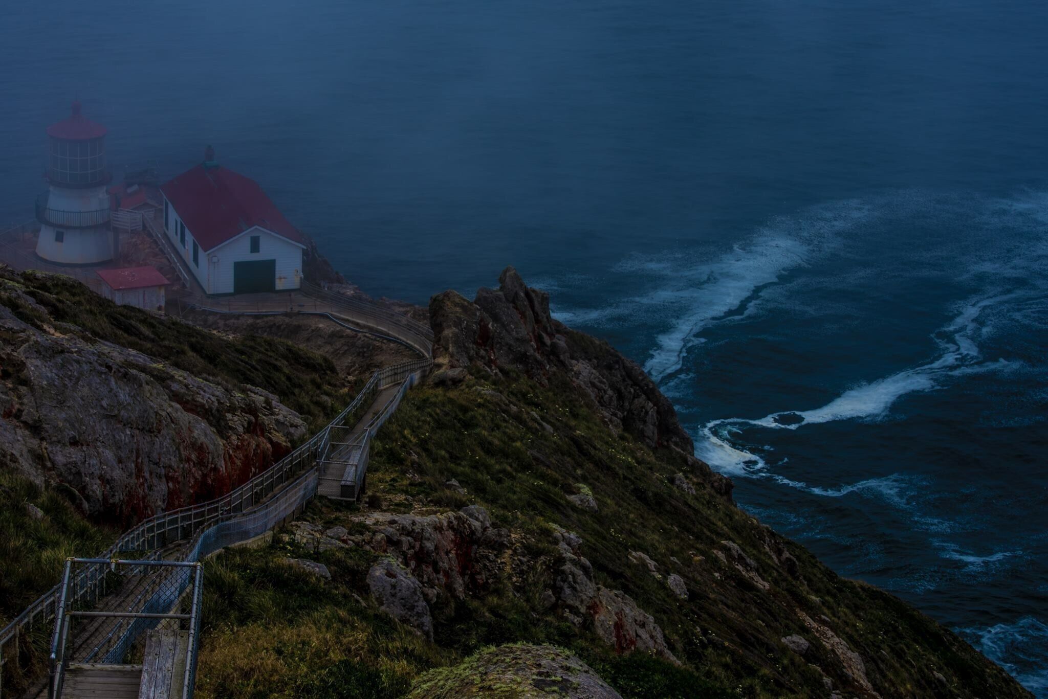 A coastal lighthouse and a wooden staircase leading down to the sea.