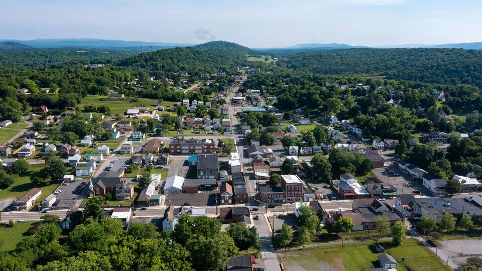 A small town with a central road, surrounded by green hills and dense forests.