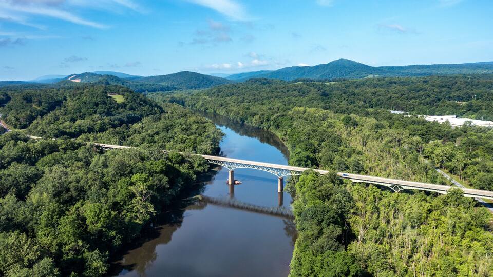 A bridge over a river surrounded by dense forest and hills.