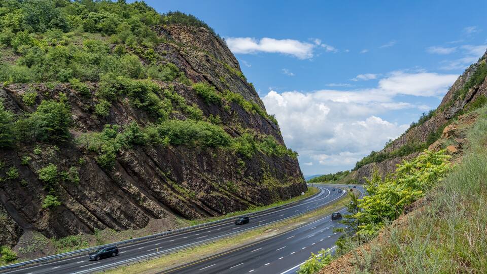 A highway curving through a mountainous landscape with lush greenery and rocky cliffs.