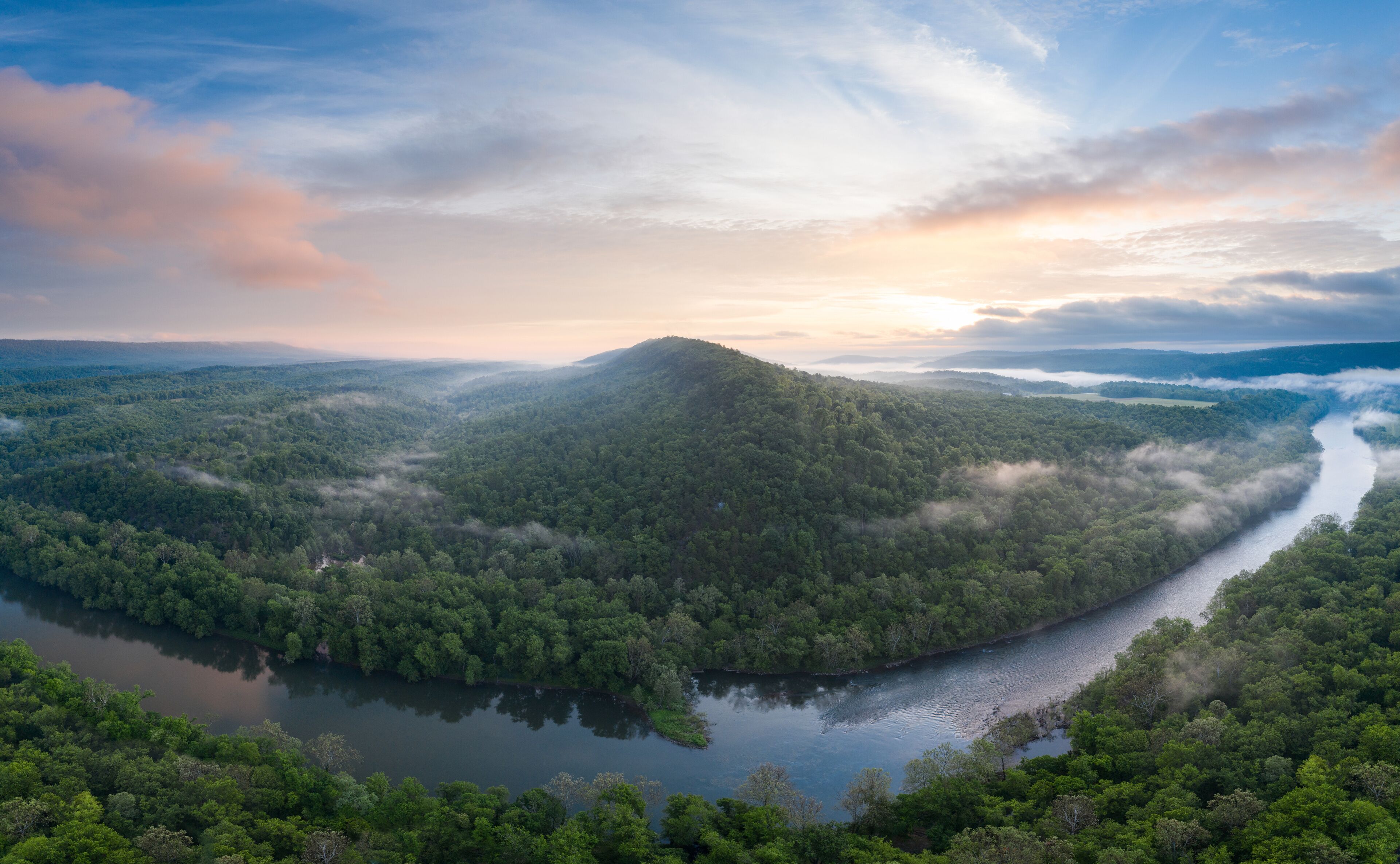 A river winding through a dense forest with a mountain in the background.