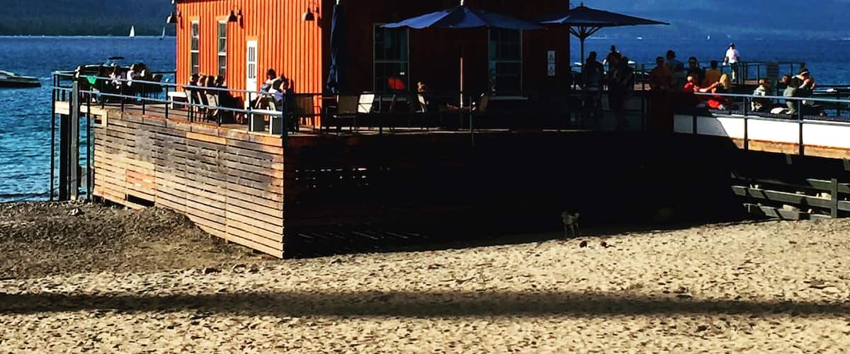 A wooden building with a red exterior and a flagpole, located on a beach with people sitting outside.