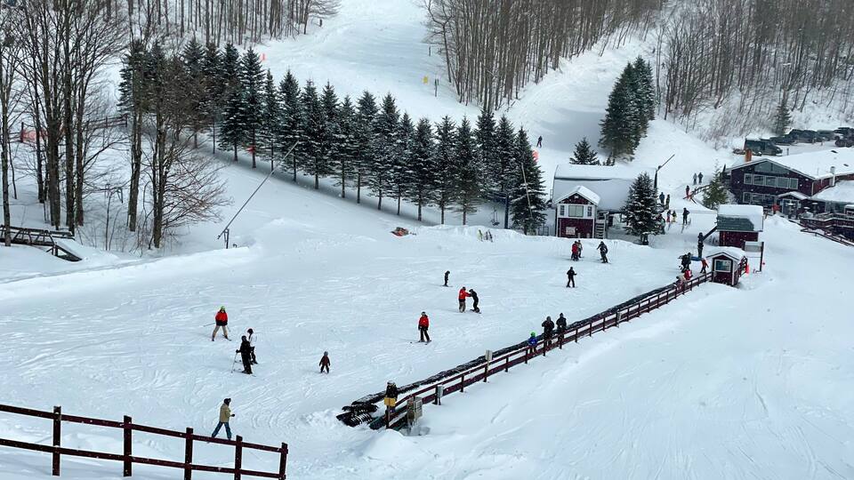 A snowy ski slope with skiers, a wooden fence, and a small cabin.