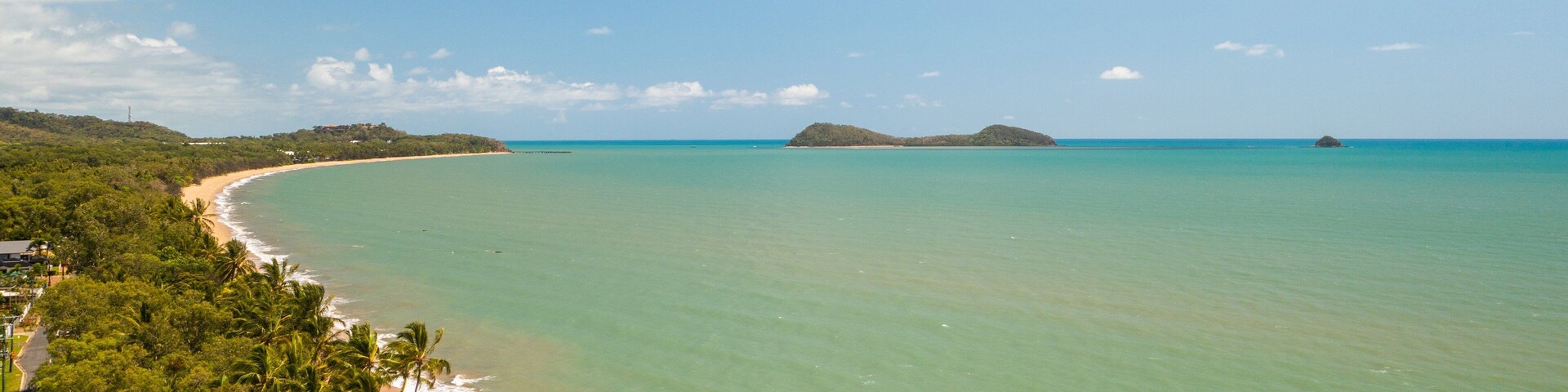 Una playa tropical con aguas turquesas cristalinas, una orilla de arena y abundante vegetación.
