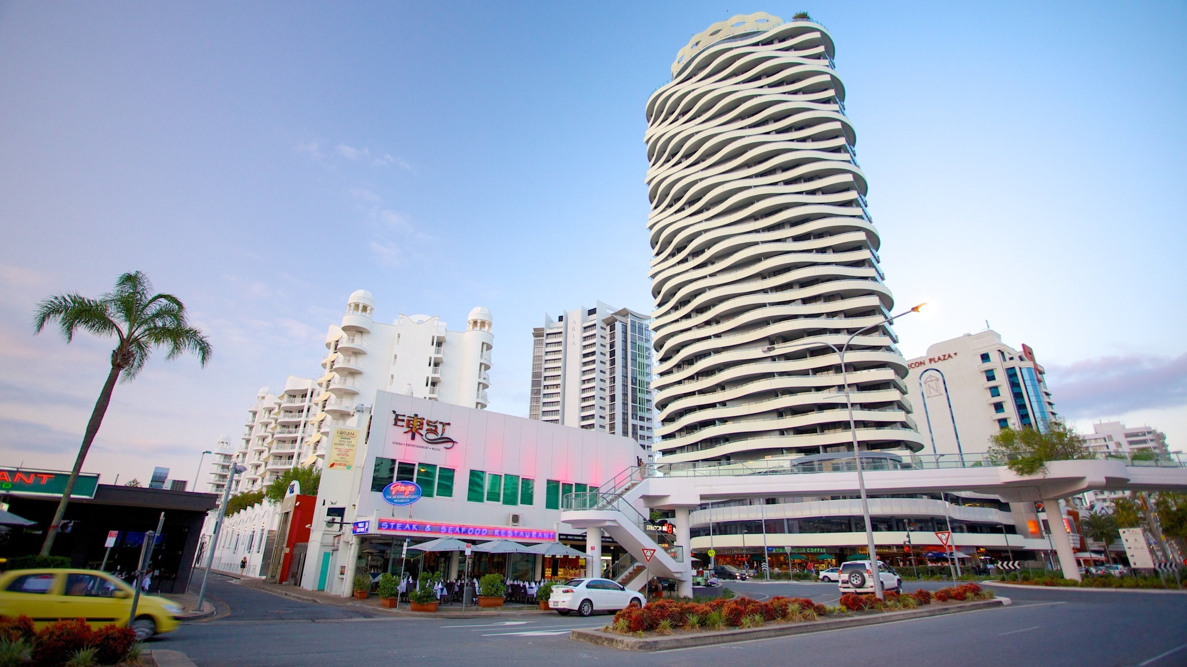 Una calle urbana moderna con una torre espiral distintiva, un restaurante de carne y mariscos, y varios edificios comerciales.