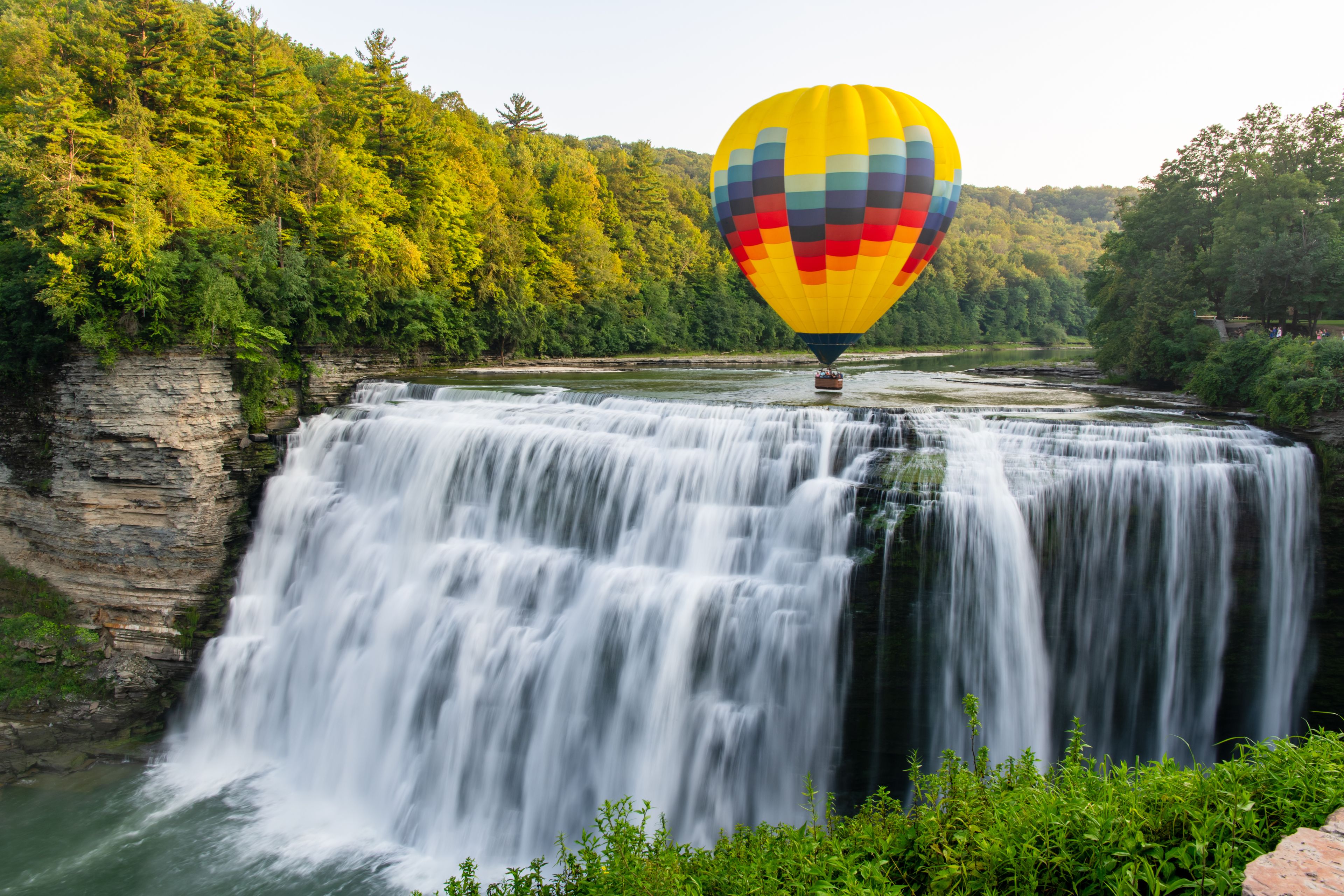 A hot air balloon flying low over the middle falls at Letchworth State Park in New York. The falls are shown in long exposure. 