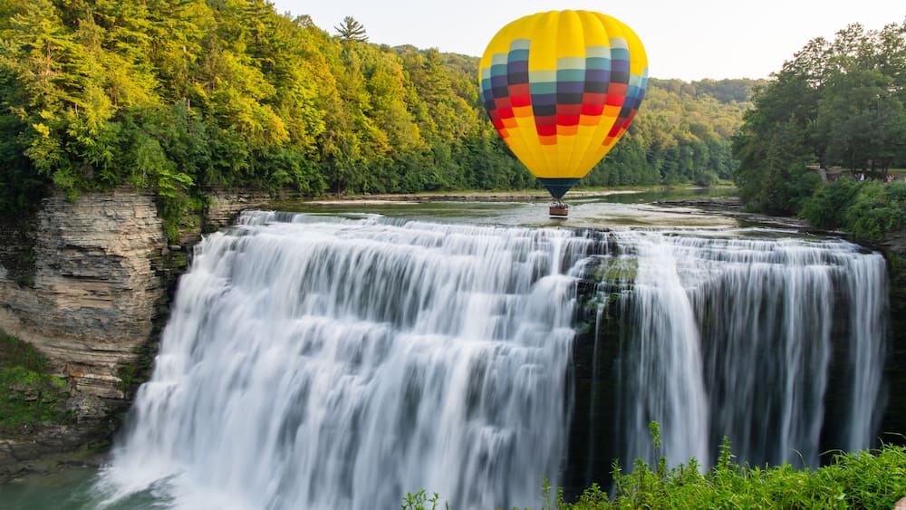 A hot air balloon flying low over the middle falls at Letchworth State Park in New York. The falls are shown in long exposure.