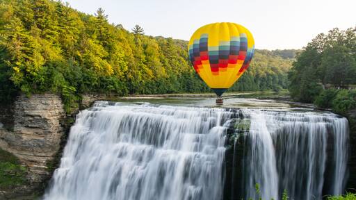 A hot air balloon flying low over the middle falls at Letchworth State Park in New York. The falls are shown in long exposure.