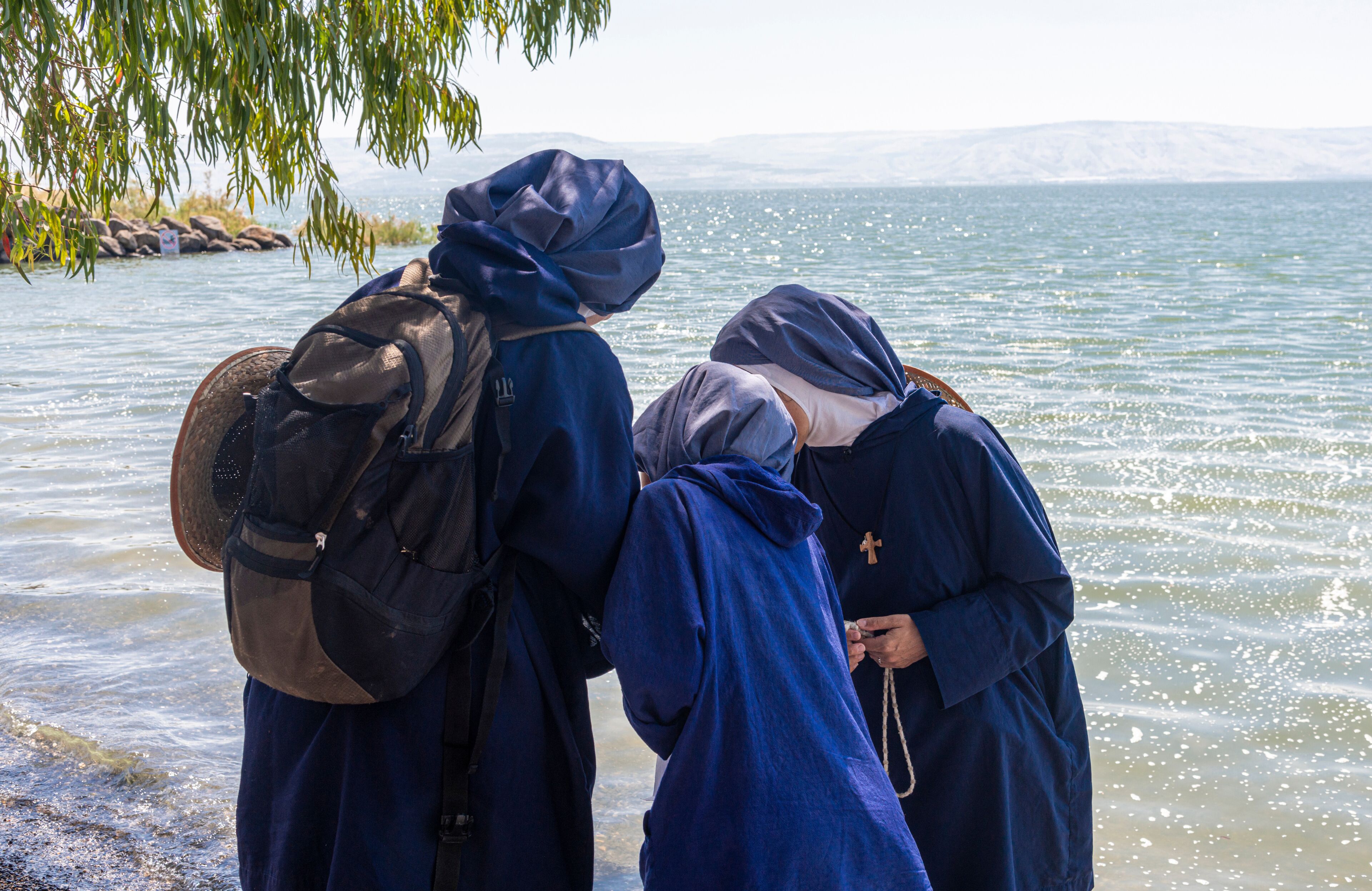 Dos personas vestidas de azul junto a un cuerpo de agua con montañas al fondo.