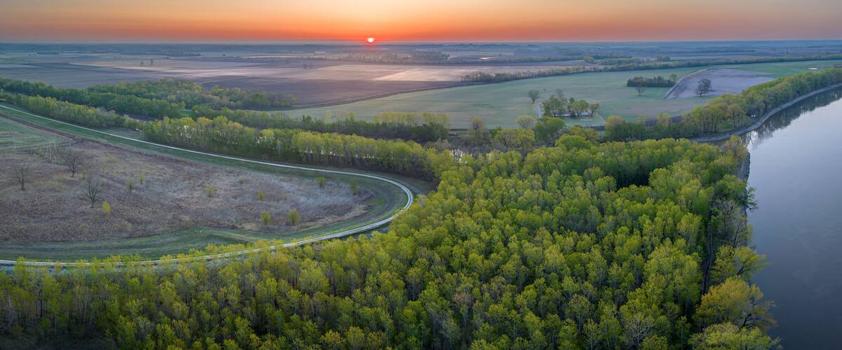 A winding road through a forested area with a sunset in the background.