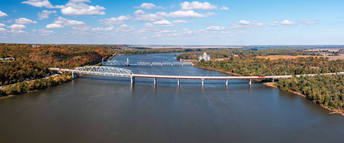 A bridge over a river with autumn foliage and industrial structures in the background.