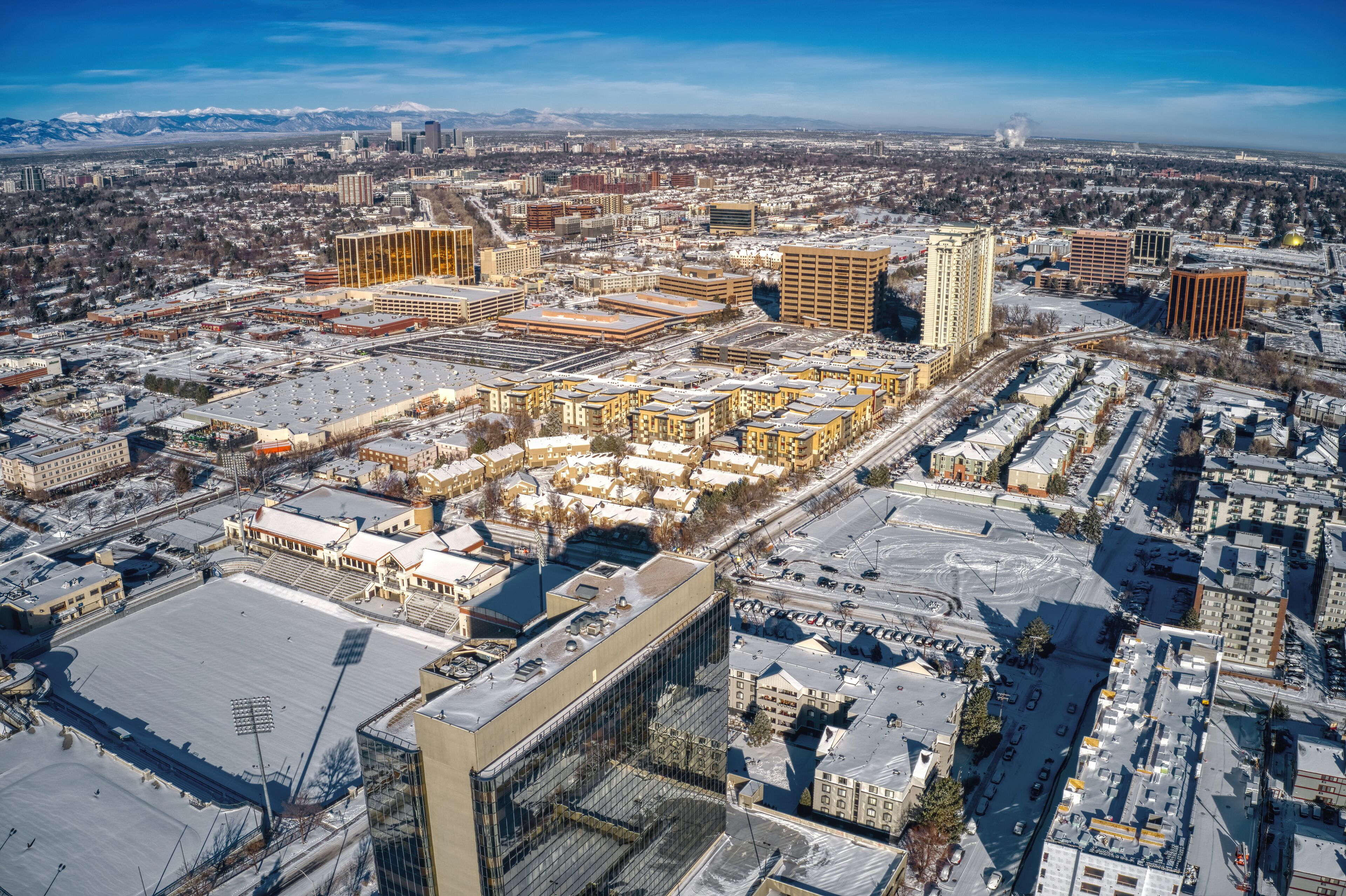 An aerial view of a city with snow-covered streets and buildings, including a large sports stadium and several high-rise buildings.