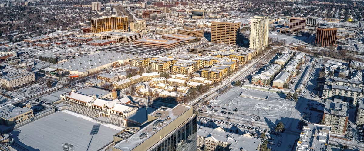 An aerial view of a city with snow-covered streets and buildings, including a large sports stadium and several high-rise buildings.