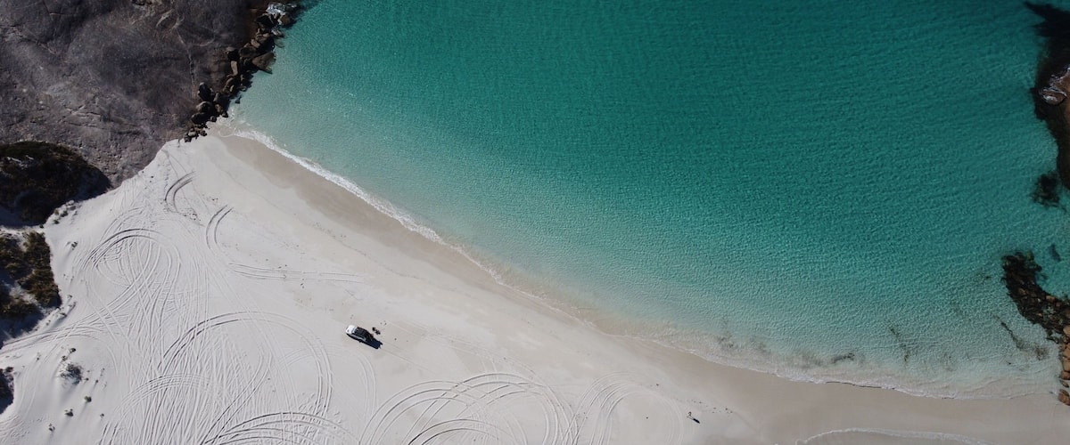 A sandy beach with clear turquoise water and a small boat near the shore.