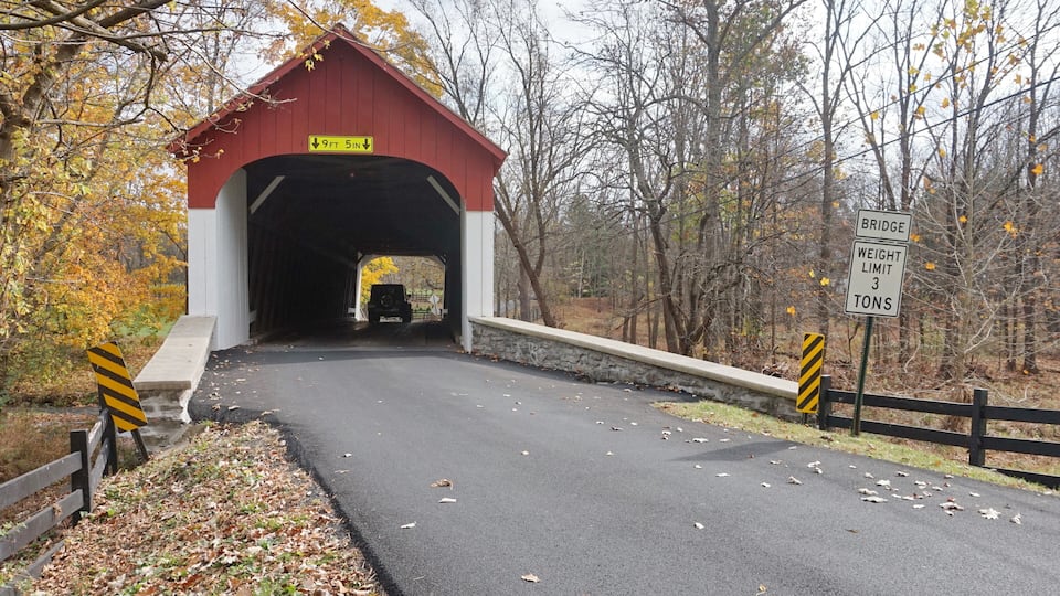 A covered bridge with a weight limit sign, surrounded by autumn foliage.