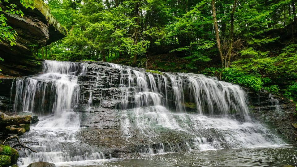 A multi-tiered waterfall surrounded by dense forest.