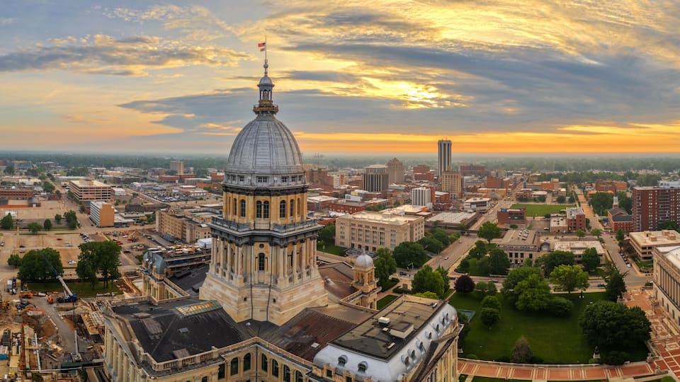 A cityscape with a prominent dome building, a tall tower, and a sunset sky.