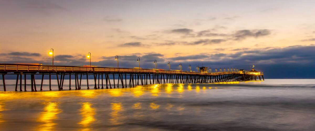A long pier with lights extending into the water at sunset.