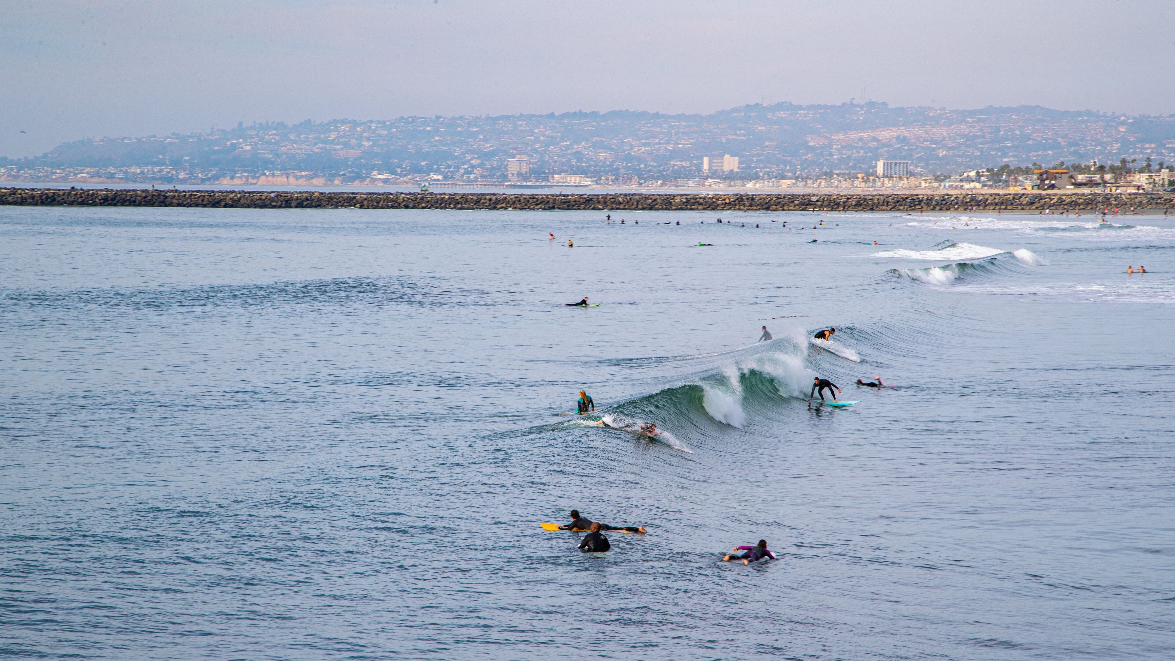 Surfers riding waves in a coastal area with a distant cityscape.