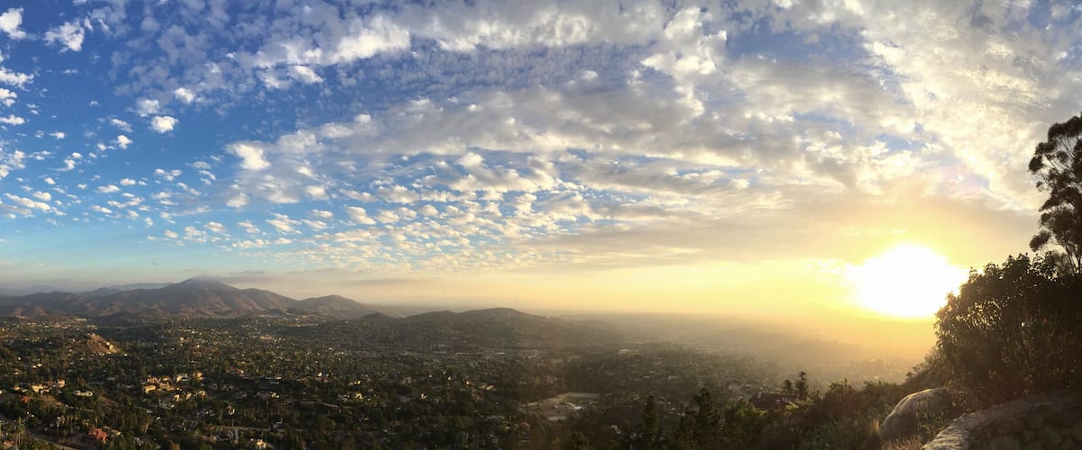 A panoramic view of a city with mountains in the distance and a partly cloudy sky.