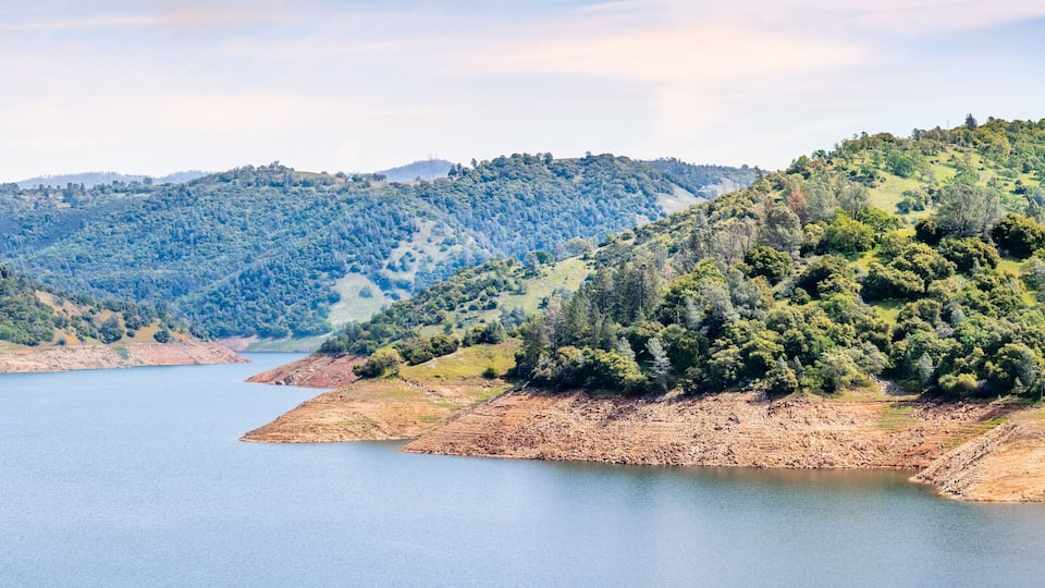 A lake surrounded by hills with dense forests and a clear sky.