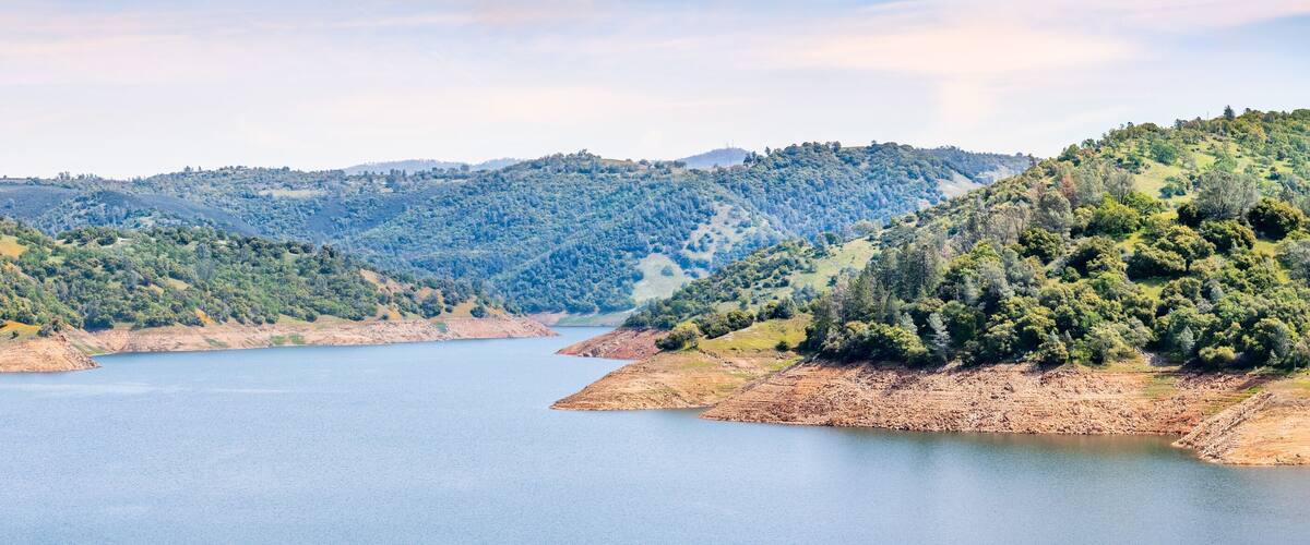 A lake surrounded by hills with dense forests and a clear sky.