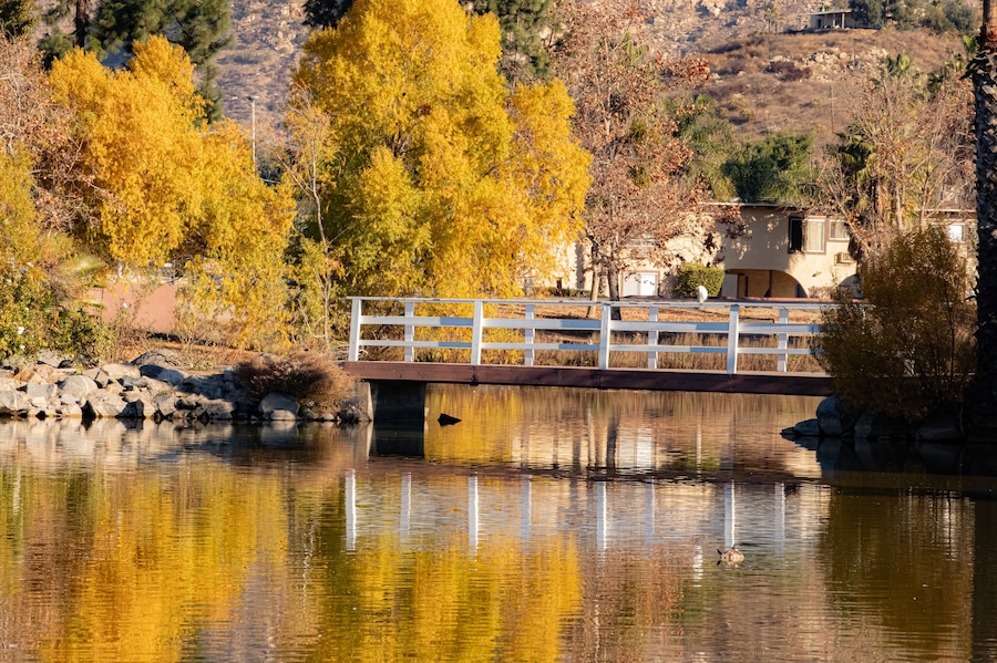 A bridge over a calm river with autumn-colored trees reflecting in the water, surrounded by hills.