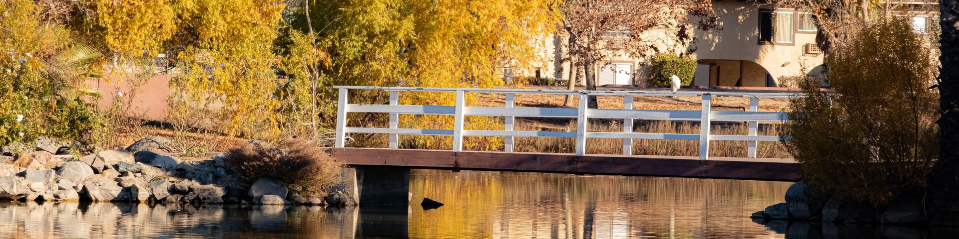 Un puente sobre un río tranquilo con árboles de colores otoñales que se reflejan en el agua, rodeado de colinas.