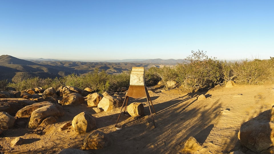 Un terrain rocailleux avec un panneau indicateur en métal, au milieu d’un paysage désertique.