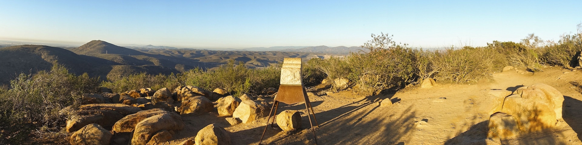 Un terrain rocailleux avec un panneau indicateur en métal, au milieu d’un paysage désertique.