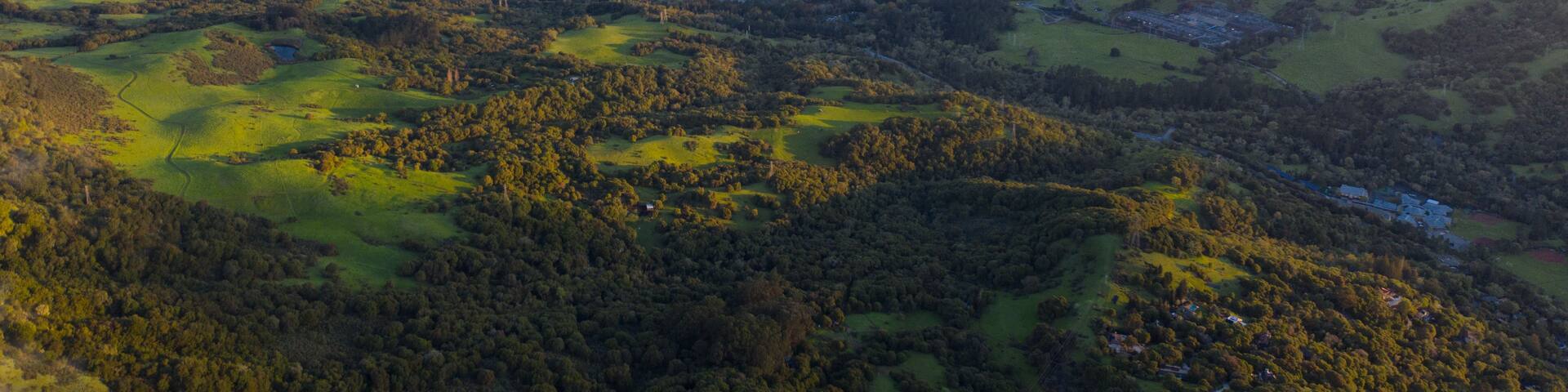 A panoramic view of a valley with a lake, surrounded by rolling hills and dense forests.