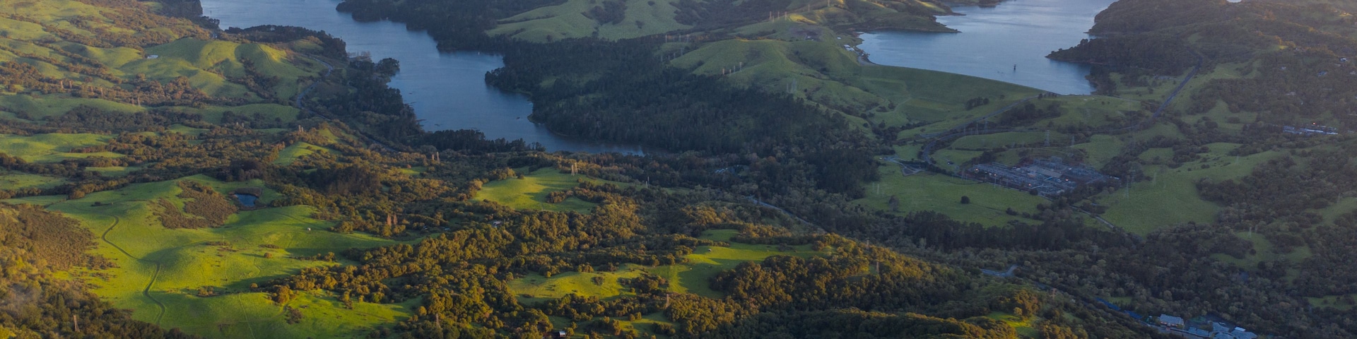 Une vue panoramique d’une vallée avec un lac, entourée de collines douces et de forêts denses.