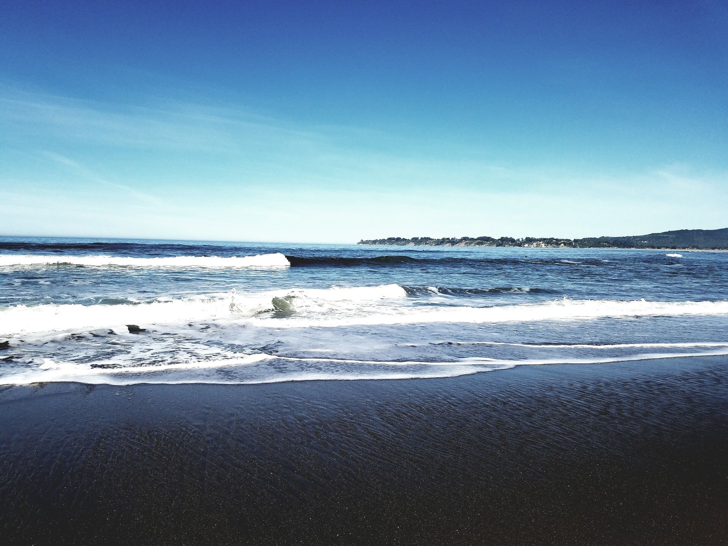 A beach with dark sand and waves crashing onto the shore.