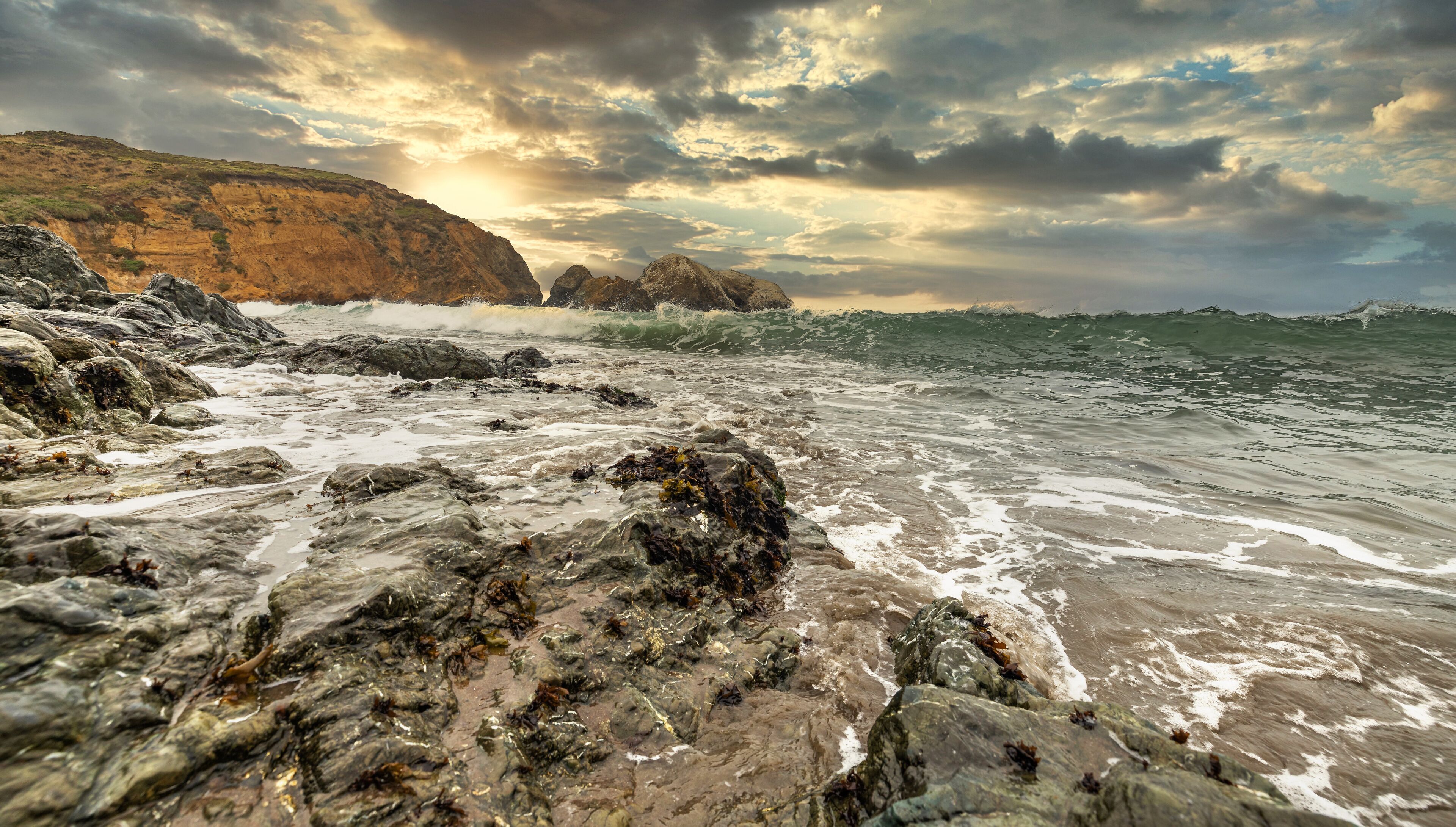 A rocky shoreline with waves crashing against the rocks under a cloudy sky.