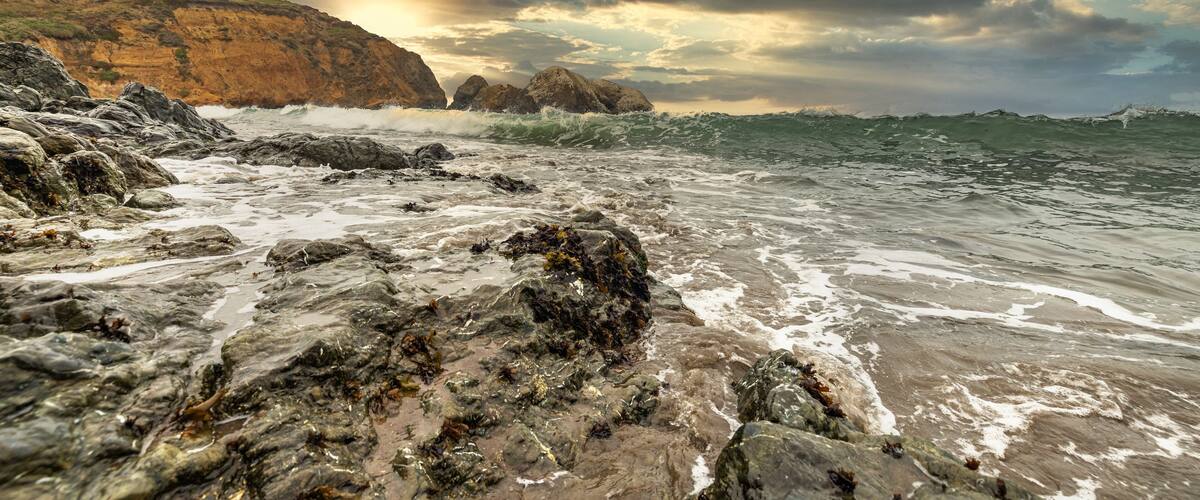 A rocky shoreline with waves crashing against the rocks under a cloudy sky.