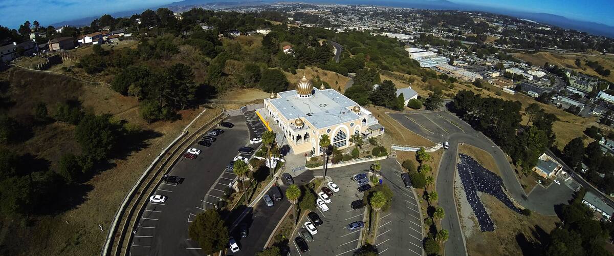 An aerial view of a city with a large parking lot, a prominent building with a dome, and surrounding hills and residential areas.