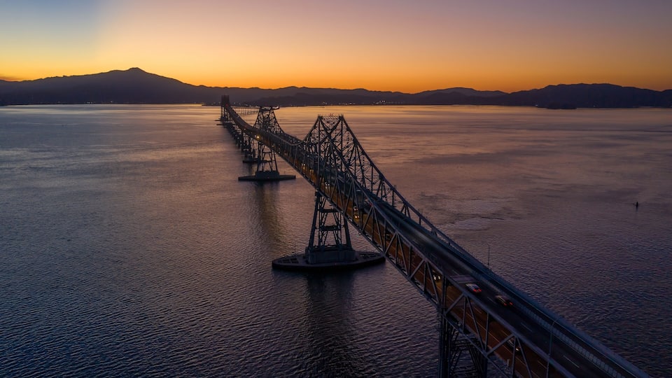 A suspension bridge over a large body of water with mountains in the background.