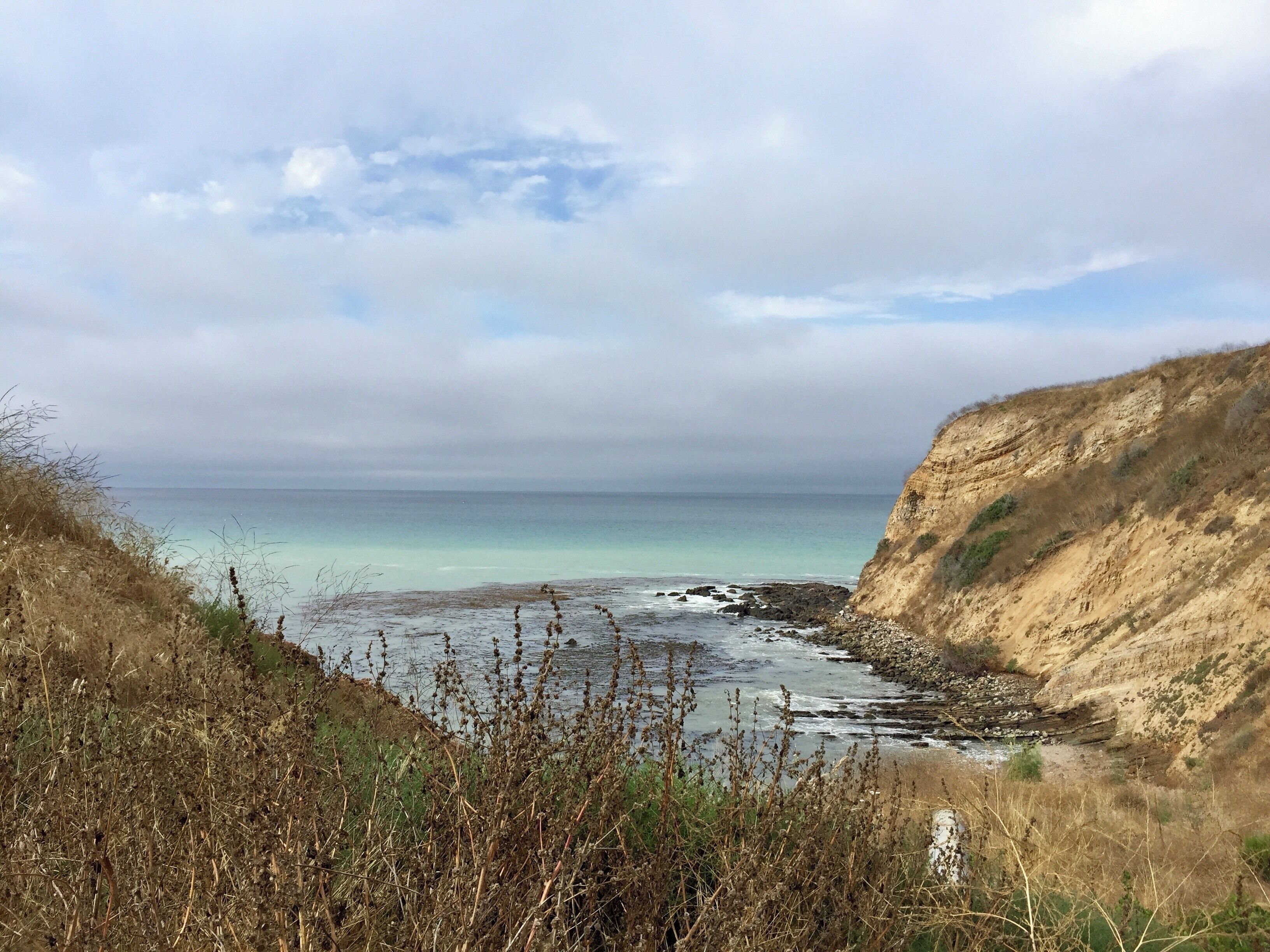 A coastal landscape with cliffs, a beach, and a calm sea under a cloudy sky.